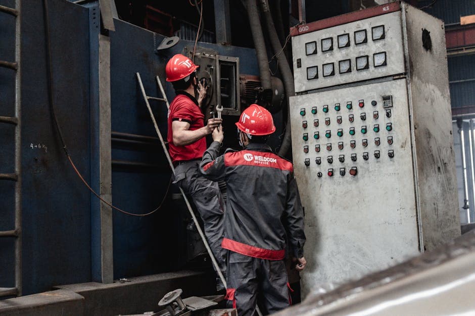 Workers in safety gear servicing industrial machinery inside a factory